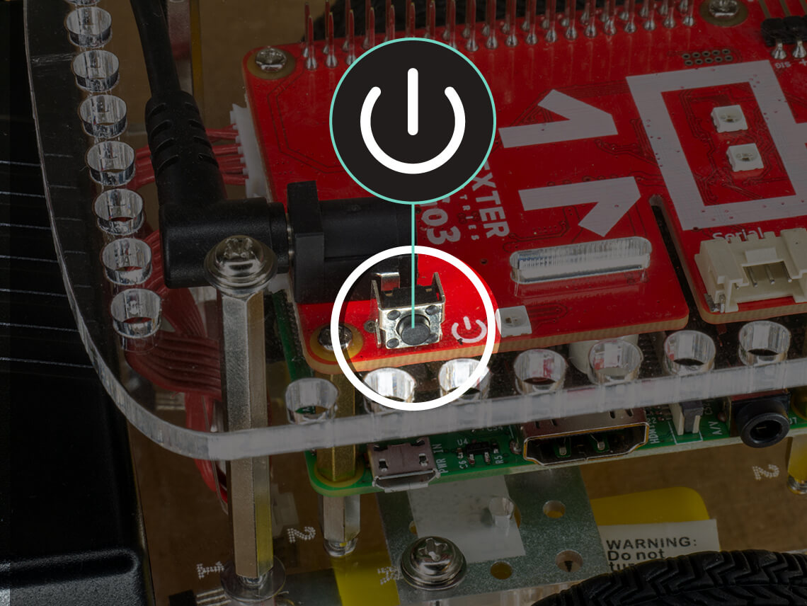 The GoPiGo power button is located near the battery power cable board on the red electronic board.